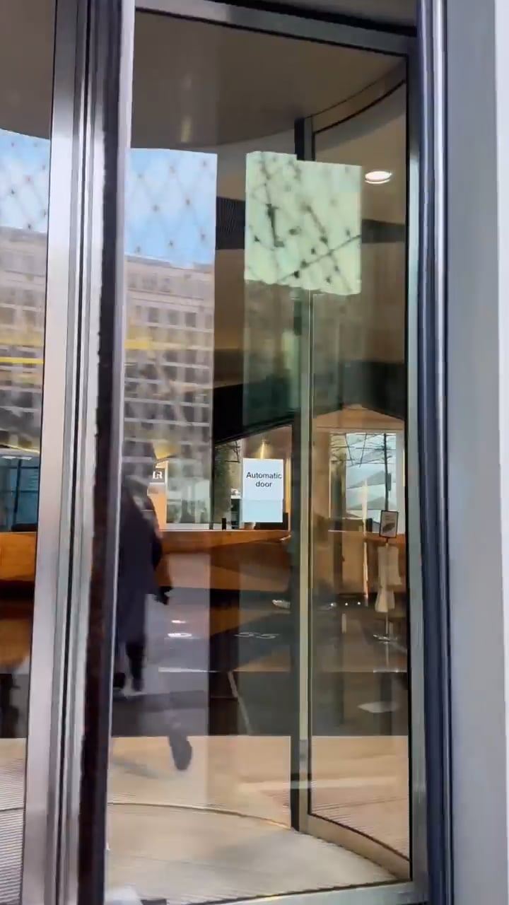 Glass automatic doors at a modern lobby, with a person exiting through a revolving entry.