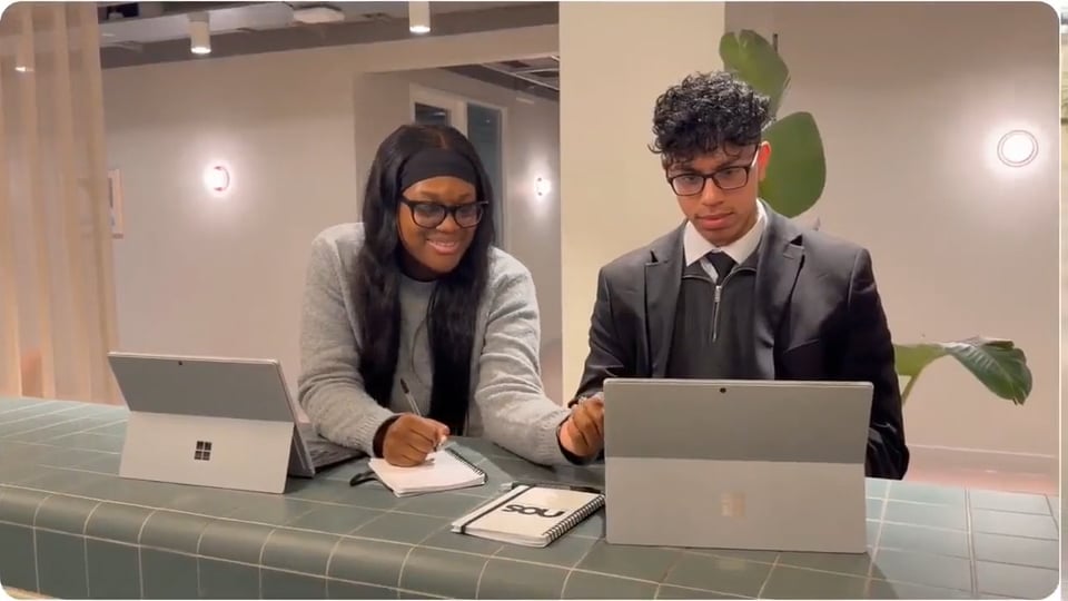 Nos › two students collaborate at a tiled counter with laptops (a microsoft surface tablet) and a notebook, smiling as they work together.