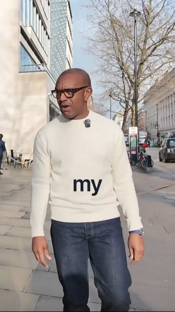 Nos › man in a white sweater with the word 'my' printed on the chest, walking down an urban sidewalk.